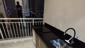 Una piccola cucina con lavandino e pensili, un balcone con ringhiera e vista sulla città di notte.