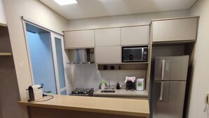 Una cucina compatta con isola centrale, due sgabelli, un forno a microonde, un frigorifero e un piano cottura a gas.