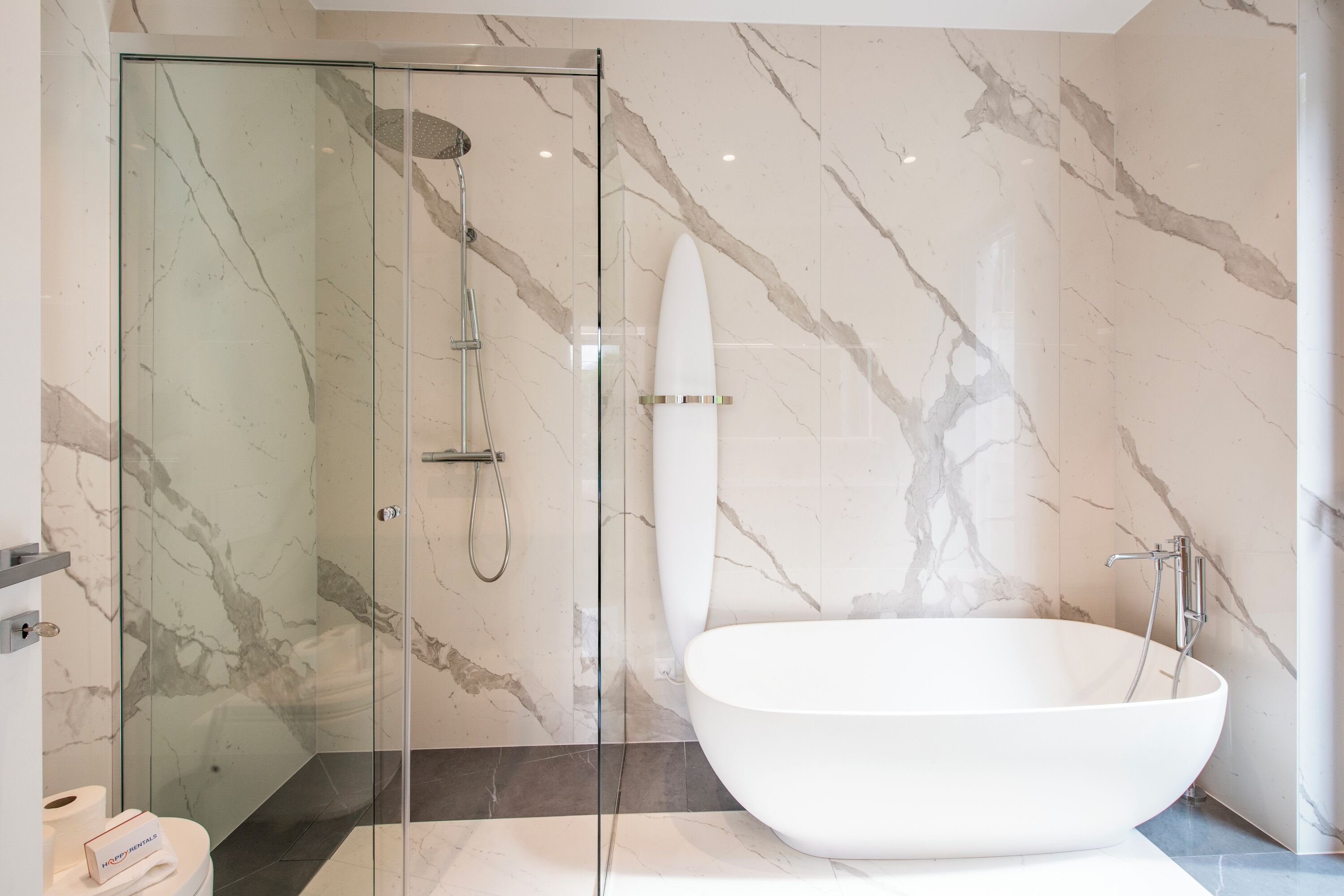 Ein modernes Badezimmer mit einer gläsernen Duschkabine, einer freistehenden Badewanne und Marmorwänden.