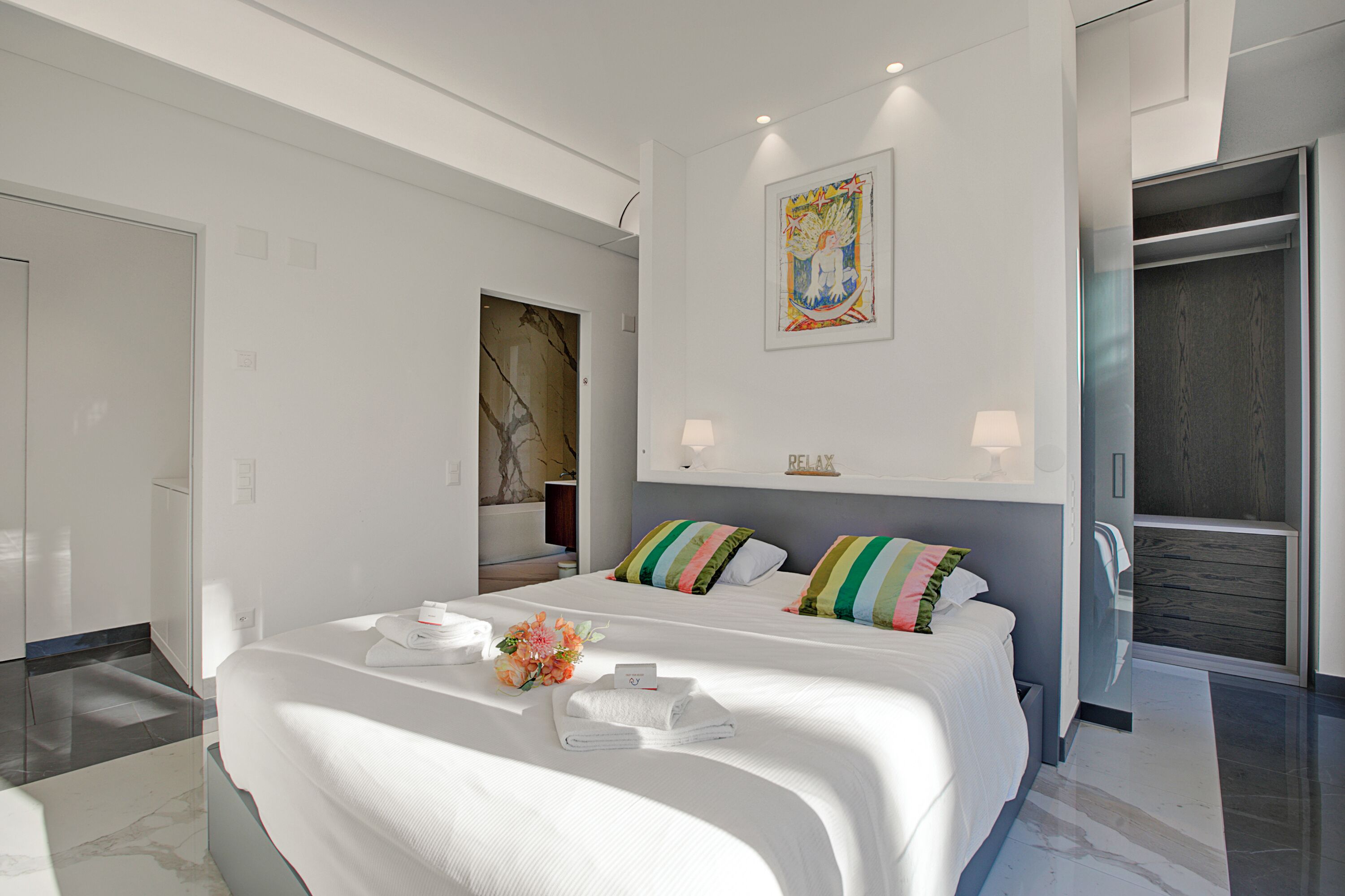 A modern hotel room with a large bed, a bathroom, and a walk-in closet.