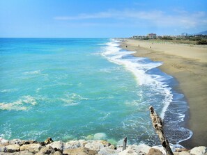 Una playa con agua turquesa cristalina, una orilla arenosa y un primer plano rocoso.