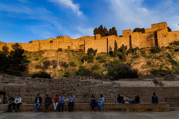 Un grupo de personas sentadas sobre escalones de piedra frente a una antigua pared de piedra bajo un cielo despejado.
