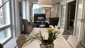 A modern dining area with a marble table, a vase of flowers, and a television in the background. - Luxury City Seafront Apartment w Balcony (Helsinki)