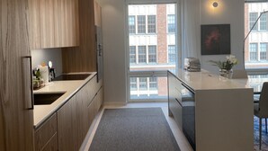 A modern kitchen with wooden cabinets, a central island, and a large window providing natural light. - Luxury City Seafront Apartment w Balcony (Helsinki)