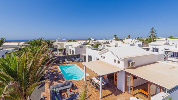 Zona de piscina en la azotea con vistas al mar, rodeada de edificios blancos y palmeras.