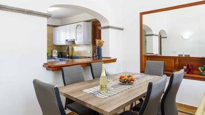 Comedor con mesa de madera, cuatro sillas grises, una botella de champán y un frutero.