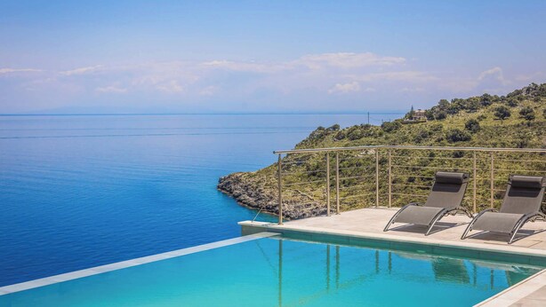 Ein Pool mit zwei Liegestühlen und Blick auf das Meer und die Hügel.