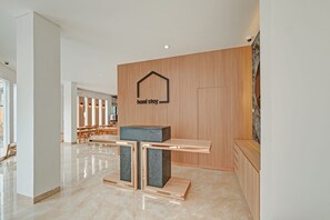 A modern hotel lobby with a reception desk, a wooden wall with a logo, and a seating area with tables and chairs. - Collection O 90774 Homi Stay (Surakarta)