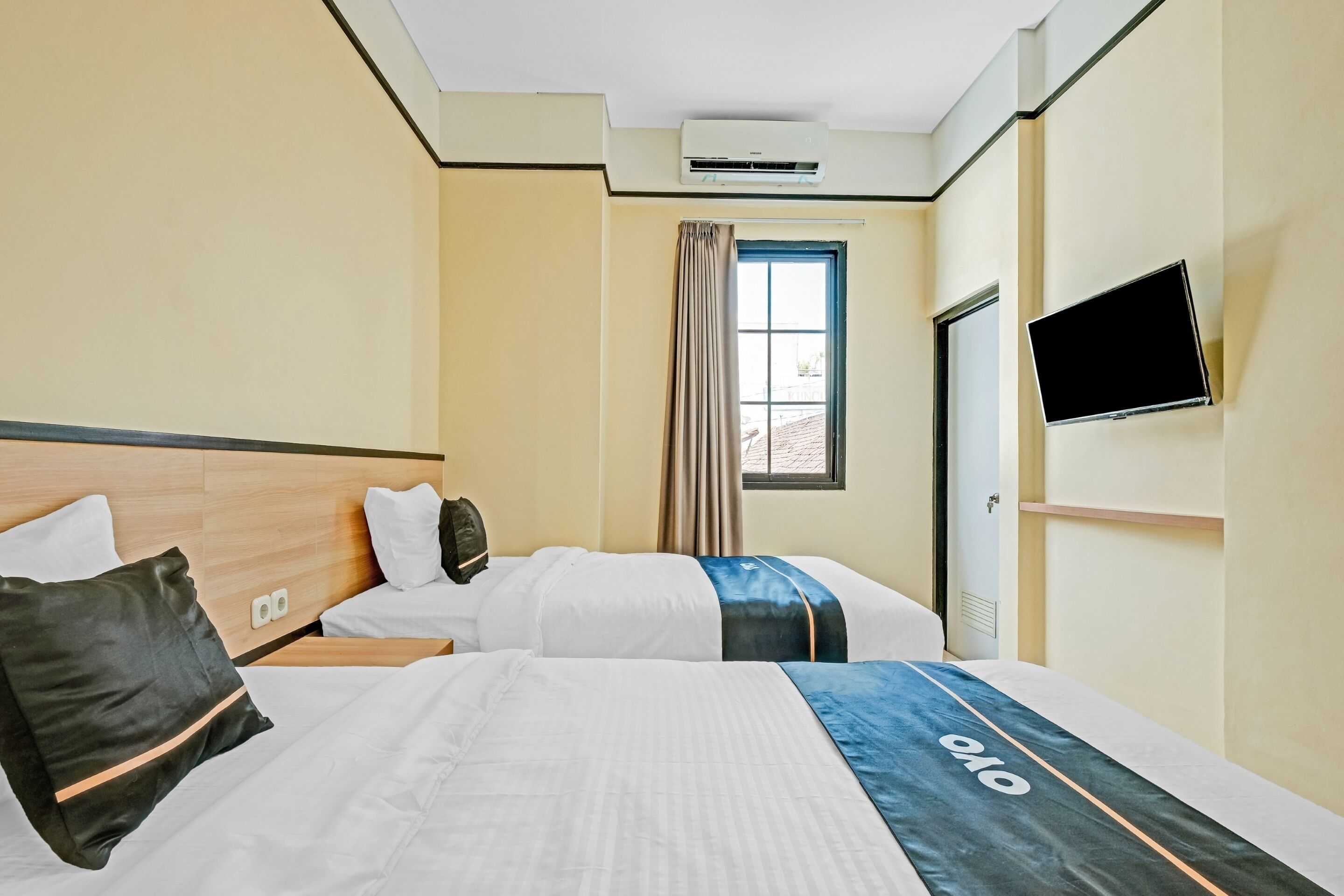 A hotel room with two beds, a TV mounted on the wall, and a window with curtains.