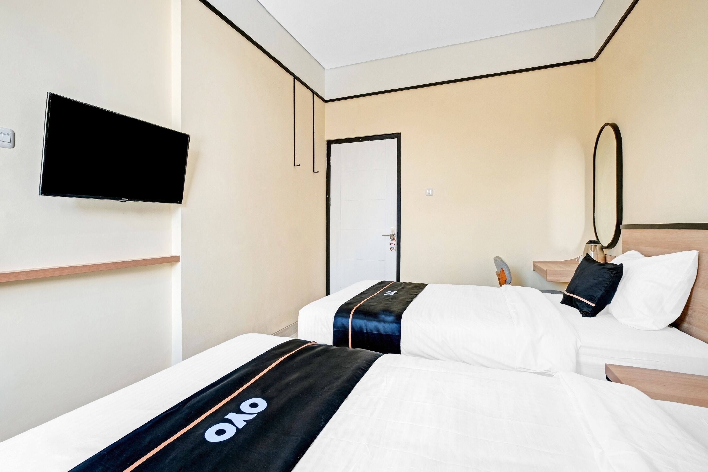 A hotel room with two beds, a TV mounted on the wall, a mirror, and a wooden nightstand.