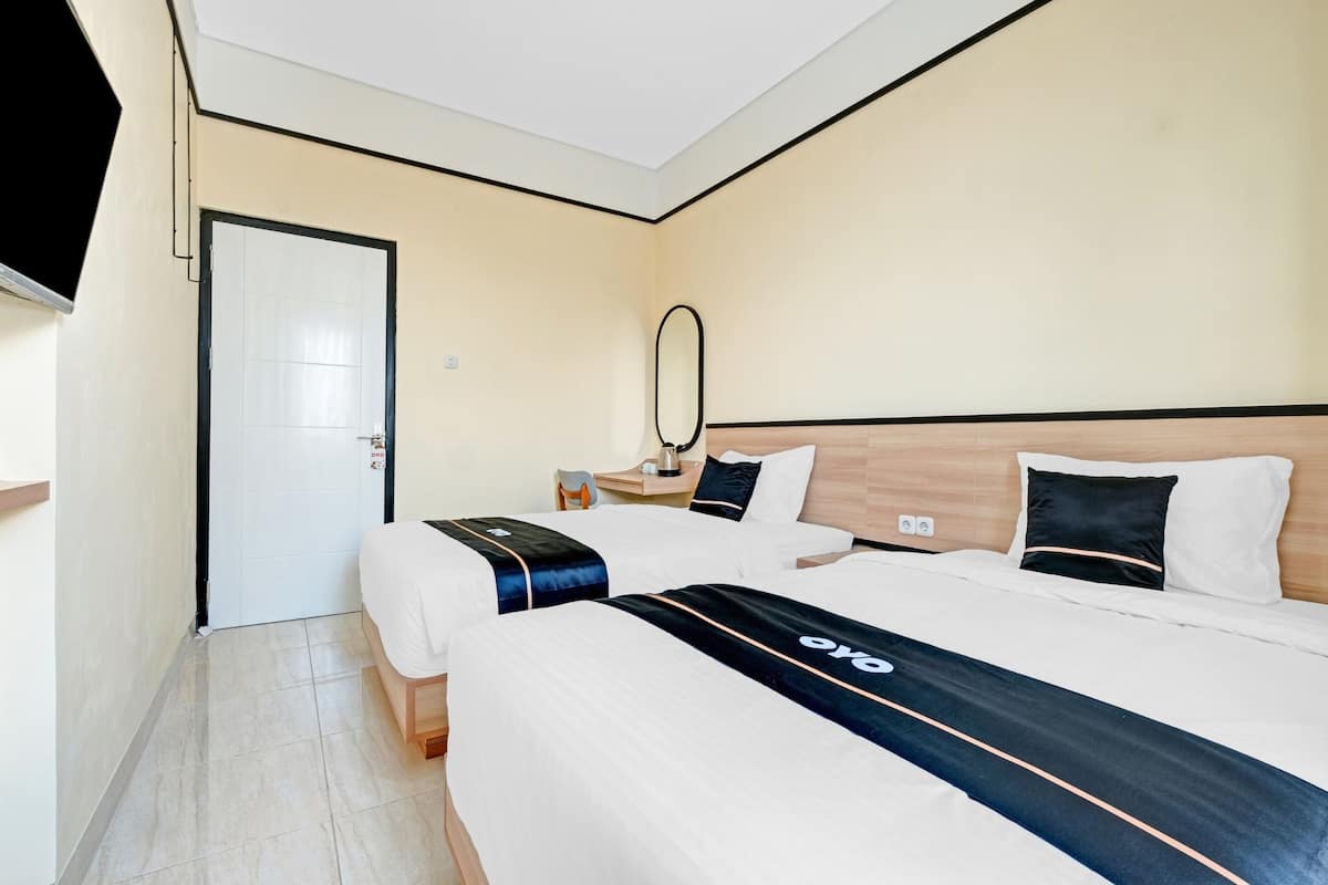 A hotel room with two beds, a wooden headboard, a bedside table with a lamp, and a mirror on the wall.