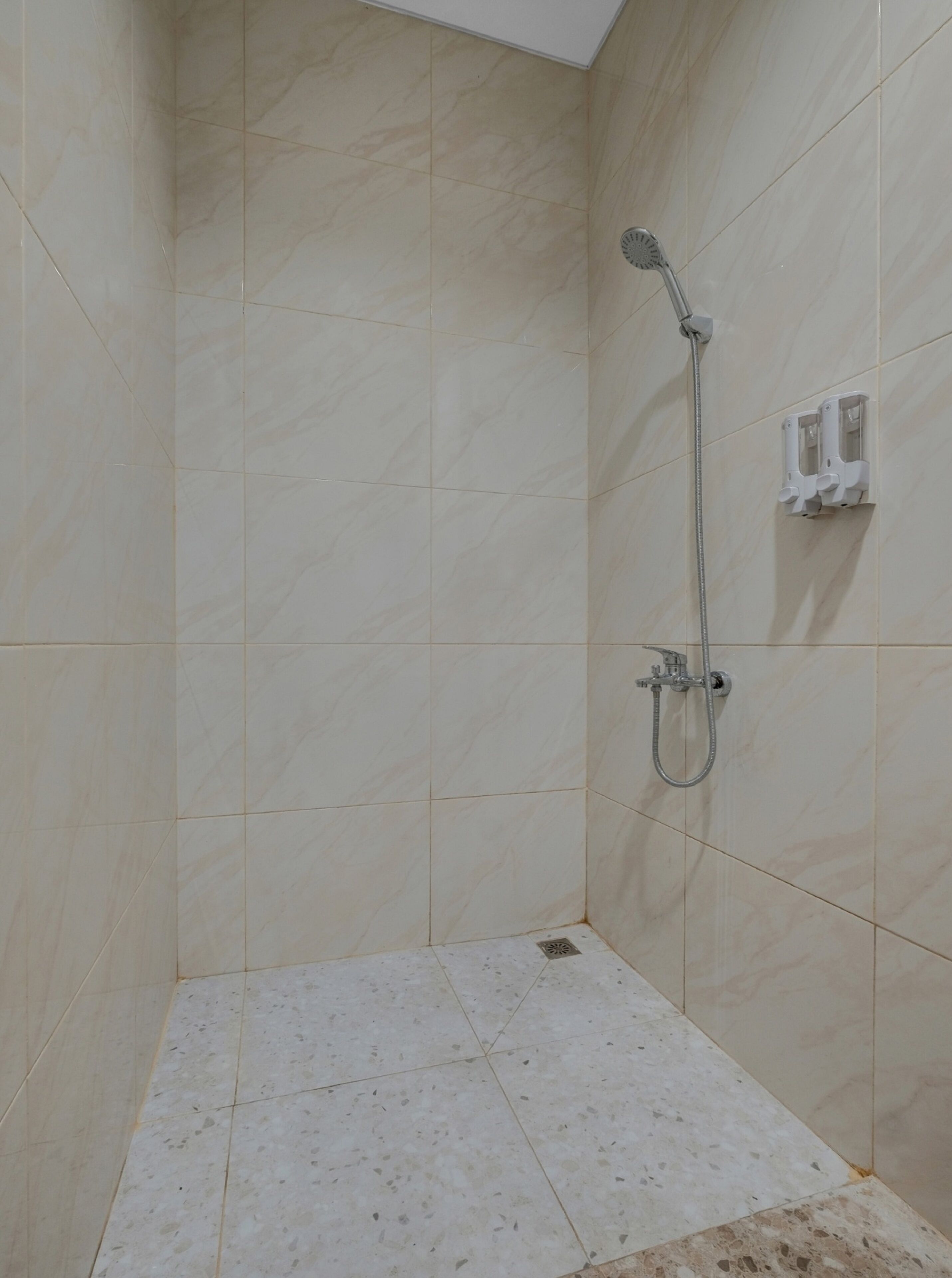 A small, tiled shower area with a handheld showerhead and a wall-mounted faucet.