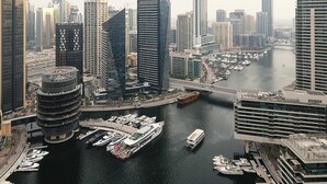 A cityscape with modern high-rise buildings, a marina with boats, and a bridge connecting two areas.