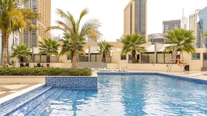 A swimming pool with blue tiles, surrounded by palm trees and modern buildings.