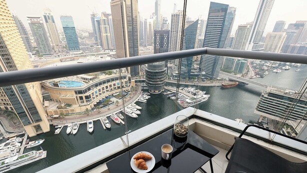 A balcony with a view of a marina and cityscape, a plate with croissants, and a cup of coffee.
