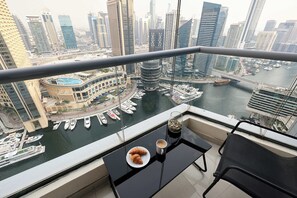 A balcony with a view of a marina and cityscape, a plate with croissants, and a cup of coffee.