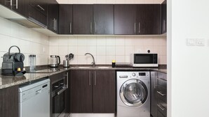 A modern kitchen with dark cabinets, a dishwasher, a washing machine, a microwave, and a coffee maker.