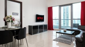 A modern living room with a dining area, a flat-screen TV, and a large window with red curtains.