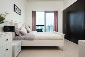 A bedroom with a bed, a nightstand, a dresser, a dark wardrobe, and a window with curtains. - Stunning Marina View 1 bedroom (Dubai)