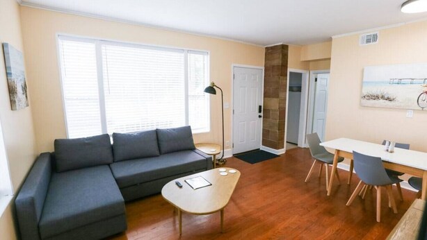 A modern living room with a grey sectional sofa, a round coffee table, and a dining area with a white table and chairs.