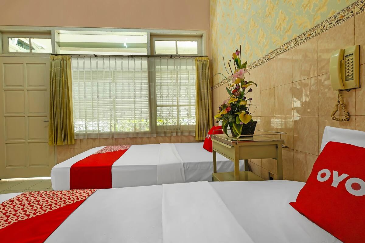A hotel room with two beds, a desk, a telephone, and a window with curtains.