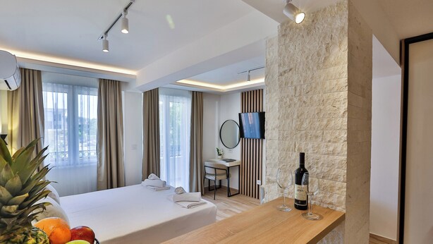 Habitación de hotel con cama, escritorio, televisor, pared decorativa de piedra y una cesta de frutas.
