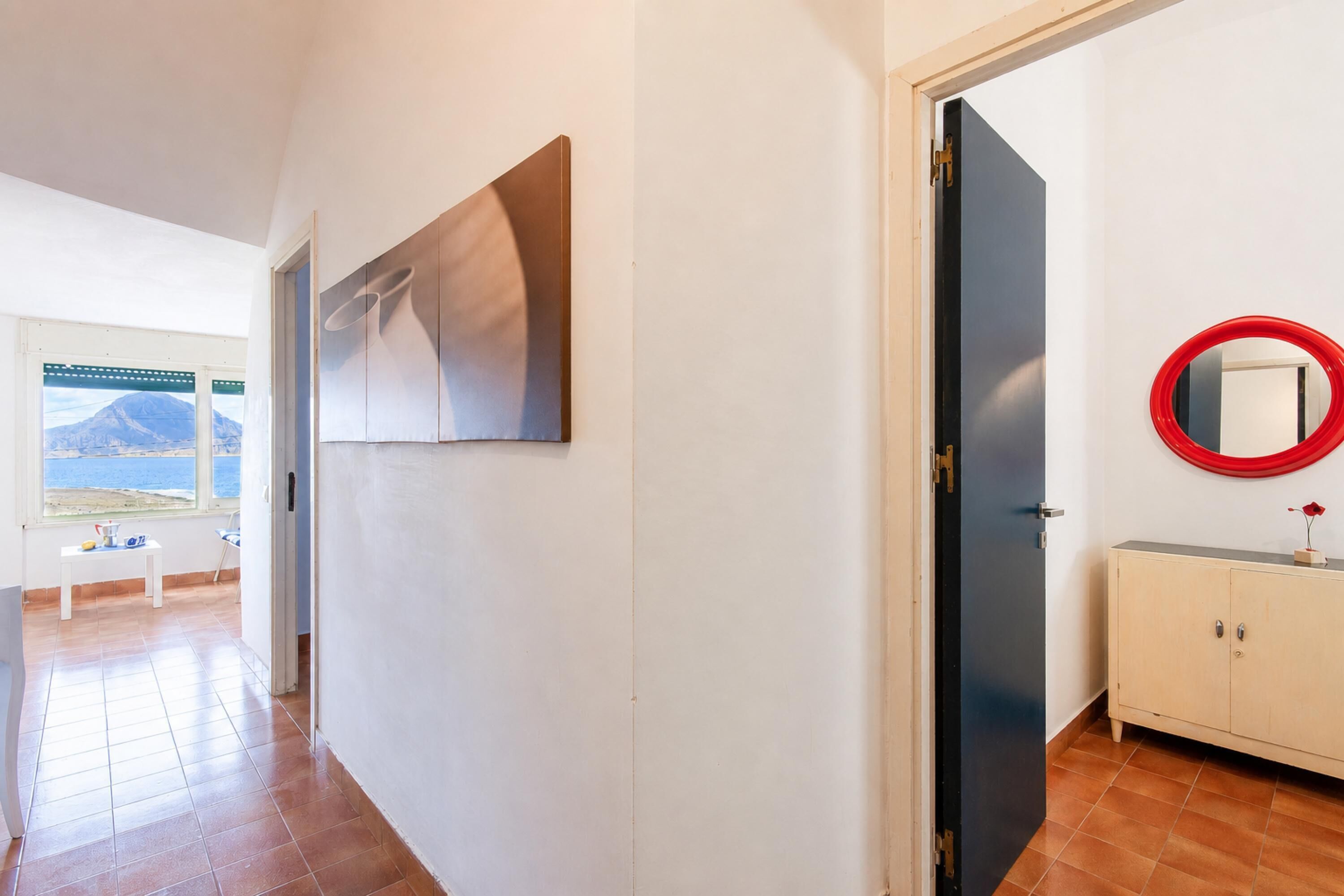 A hallway with a door, a mirror, and a view of a mountain through a window.