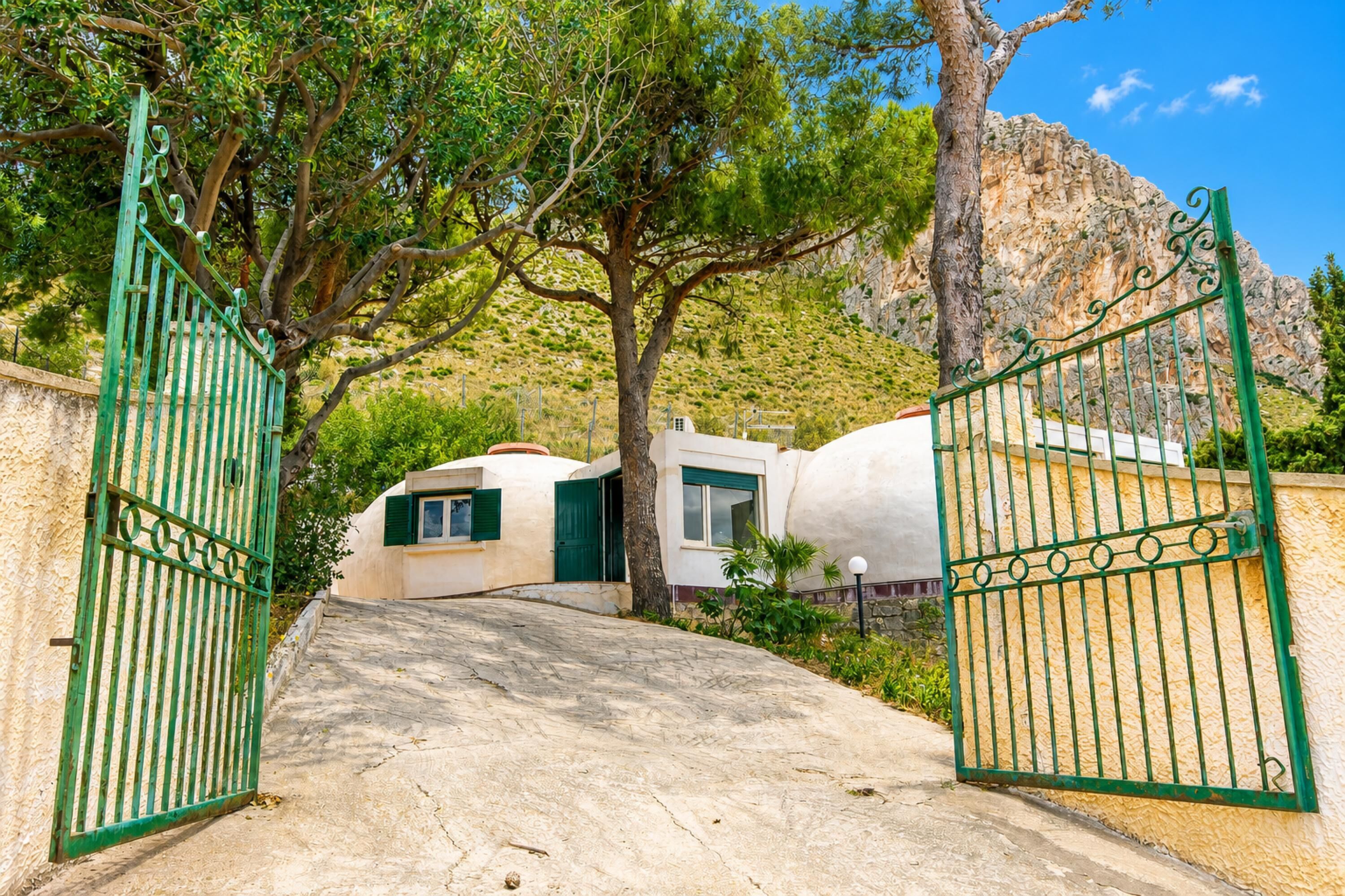 A gated entrance to a building with a stone pathway leading to a white building with green shutters.