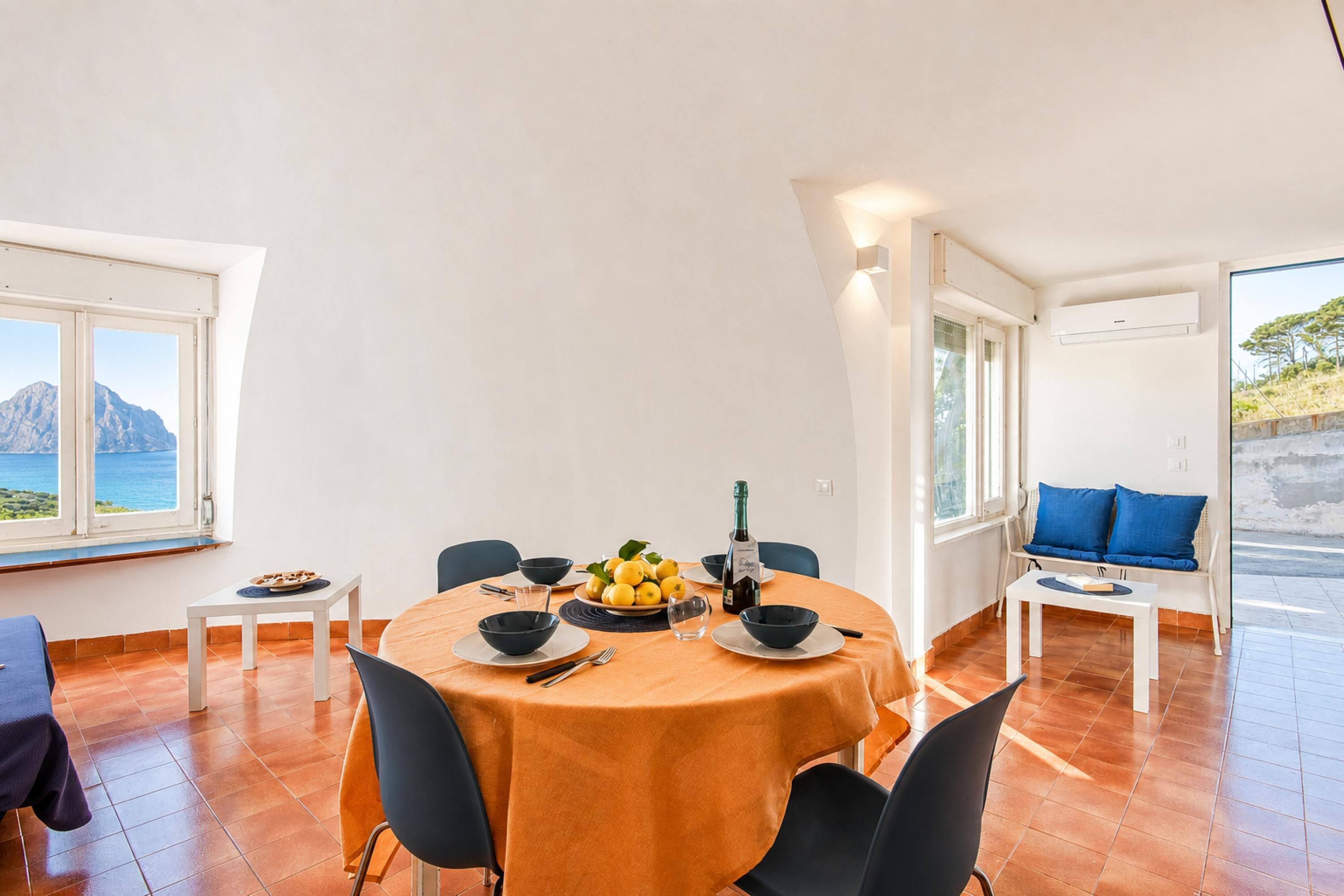 A dining area with a round table, chairs, a fruit bowl, and a bottle.
