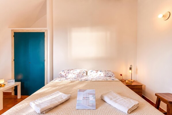 A bedroom with a bed, a nightstand, a bedside table, a blue door, and a wall-mounted light. - Villa Macari Fantastic Sea View (San Vito Lo Capo)