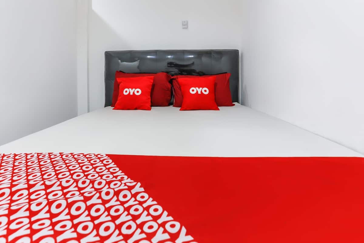 A hotel room with a white bed, red pillows, and a red patterned bedspread.