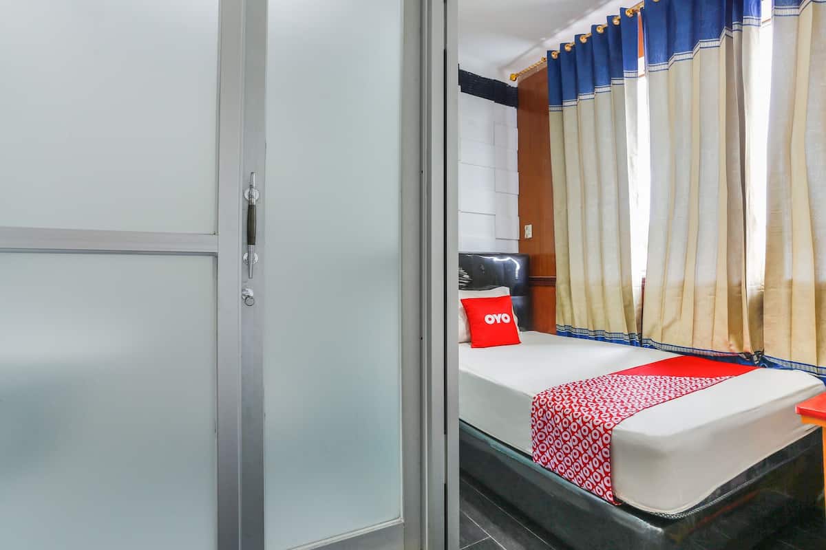 A hotel room with a bed, a red and white patterned bedspread, a red pillow with "OYO" branding, and a curtain with blue and beige colors.