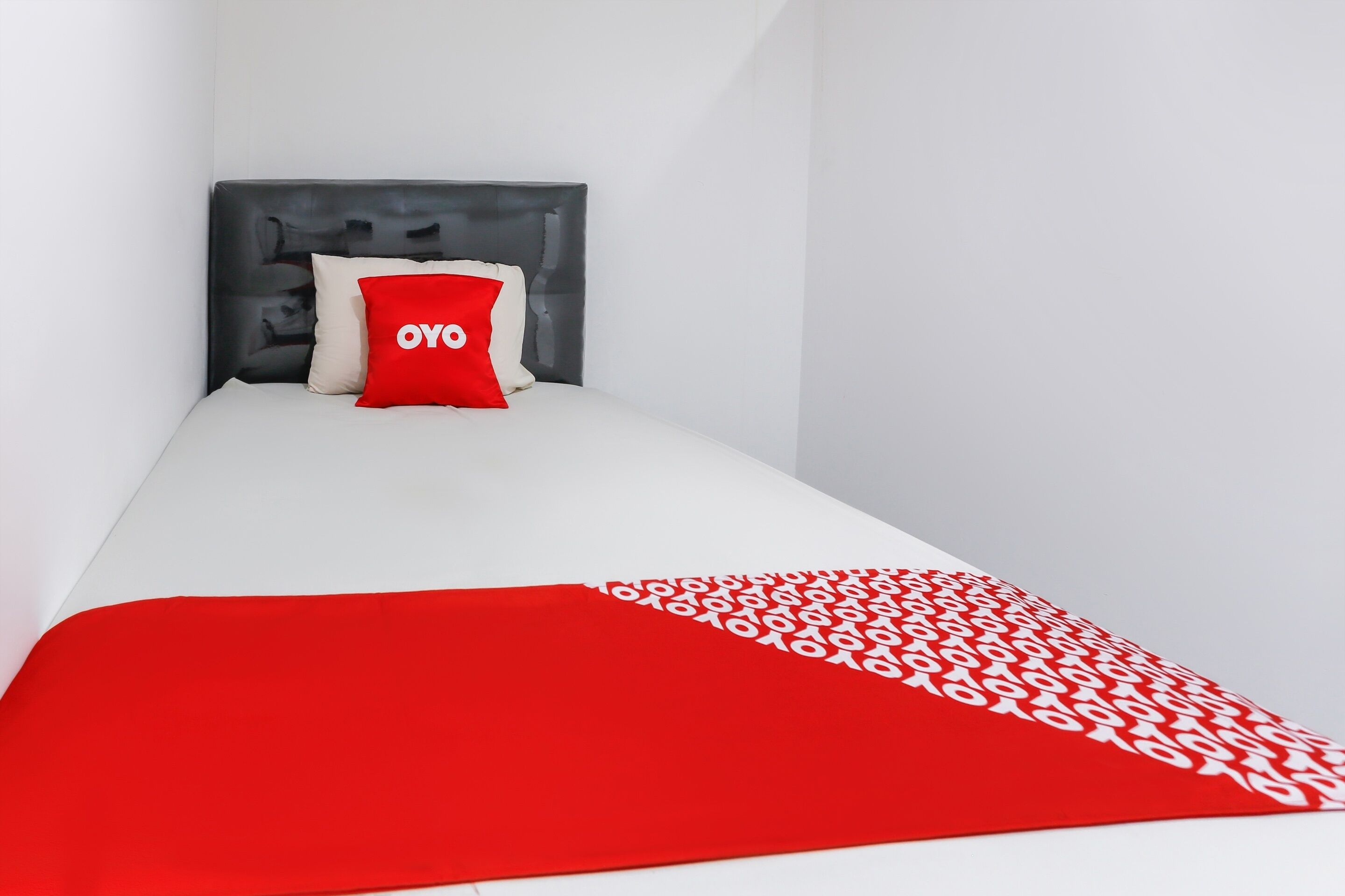 Ein kleines, ordentlich bezogenes Bett mit einem weißen Lattenrost und einer roten Decke mit weißem Muster.