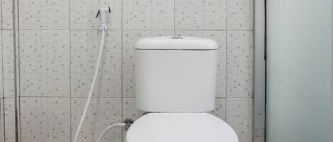 A toilet with a white tank and seat, a shower hose, and a tiled floor with a geometric pattern.
