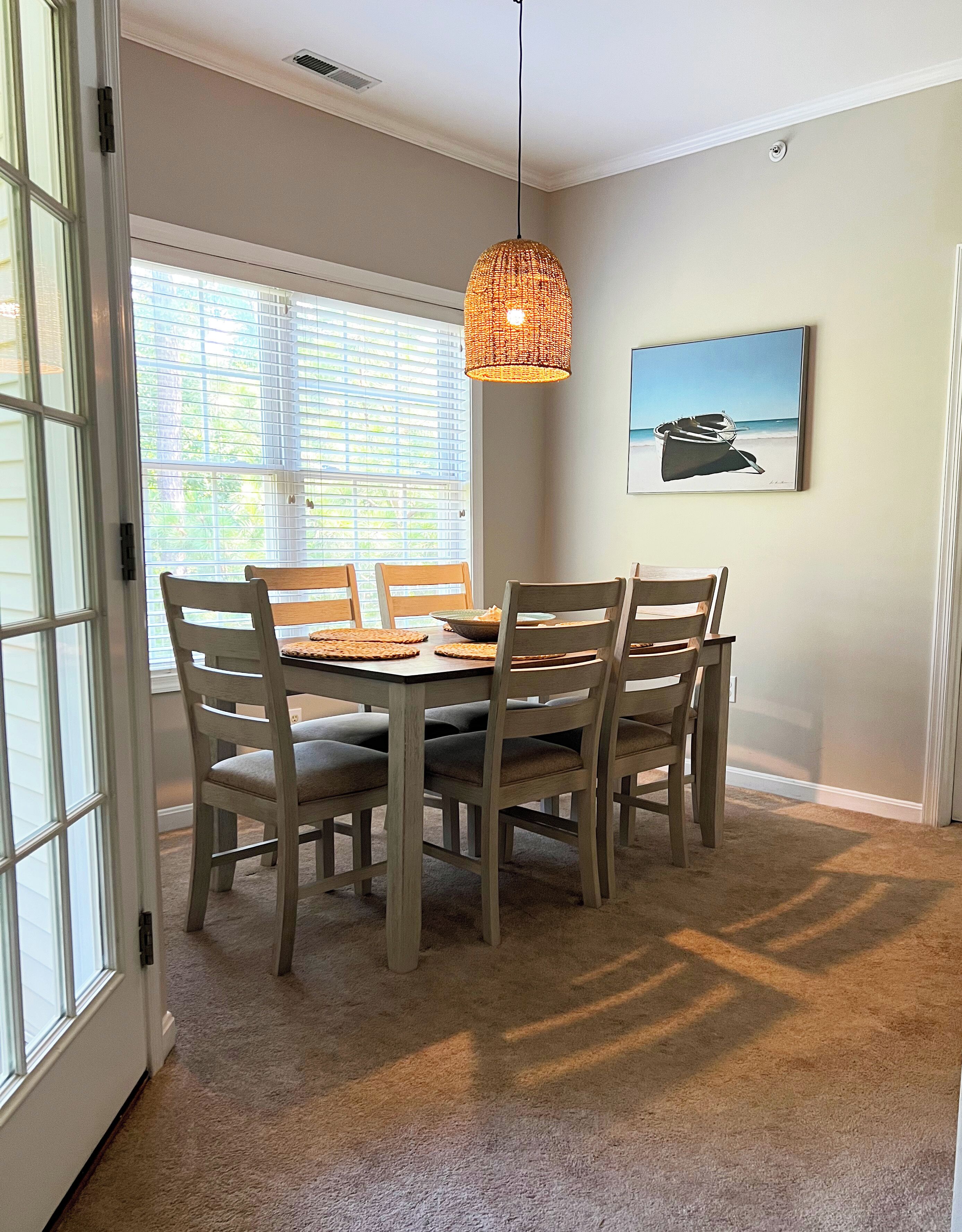 A dining area with a round table, six chairs, a hanging light fixture, and a painting on the wall.