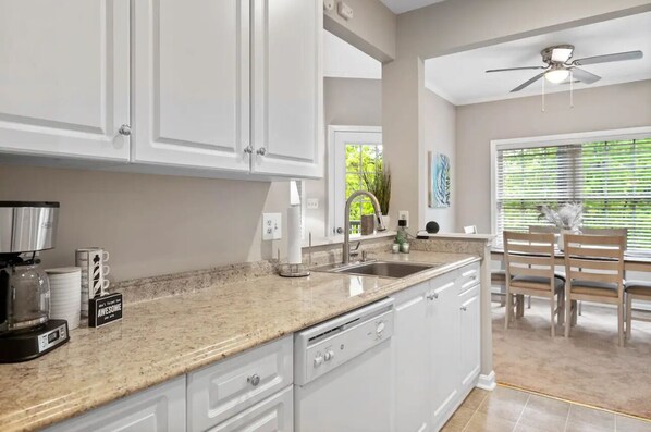 A kitchen with white cabinets, a granite countertop, a dishwasher, and a dining area with a table and chairs.