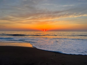 A beach with a sunset over the ocean, waves gently lapping at the shore.