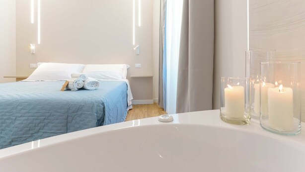 Habitación de hotel moderna con una cama grande, un baño con bañera y tres velas encendidas sobre el tocador.