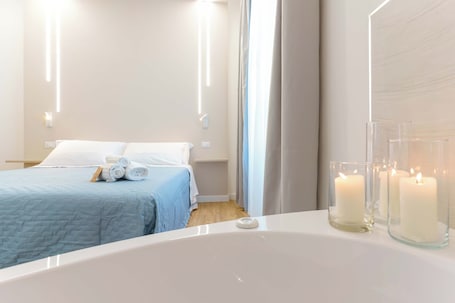 A modern hotel room with a large bed, a bathroom with a bathtub, and three lit candles on the vanity.