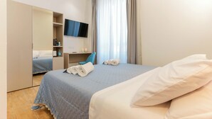Una habitación de hotel con cama, escritorio, silla, televisor y armario.