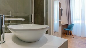 Un baño moderno con un lavabo blanco grande, cabina de ducha de vidrio y suelo de madera.