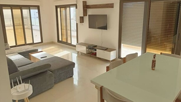 Een moderne woonkamer met een bank, een eettafel en een aan de muur bevestigde televisie.