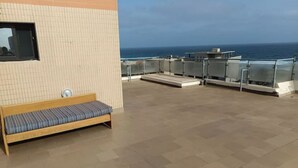 Een terras op het dak met een houten bankje en een tafeltje, met uitzicht op zee.