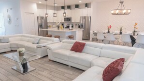 En moderne stue med en hjørnesofa, et sofabord i glas og et spiseområde med stole og bord.