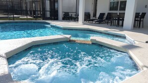 En swimmingpool med et spa-område, omgivet af liggestole og en overdækket terrasse.