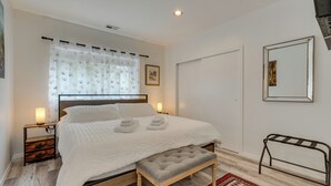 A bedroom with a bed, bedside lamps, a bench, a rug, and a mirror on the wall.