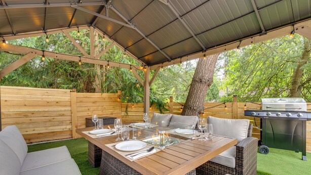 An outdoor patio with a wooden table set for dining, wicker furniture, and a barbecue grill.