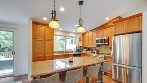 Una cocina moderna con armarios de madera, electrodomésticos de acero inoxidable, una isla grande con taburetes y lámparas colgantes.