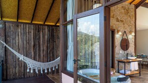 A wooden room with a hammock, a stone wall, a stone fireplace, and a view of the outdoors. - Monte Mauá Chalés (Resende)