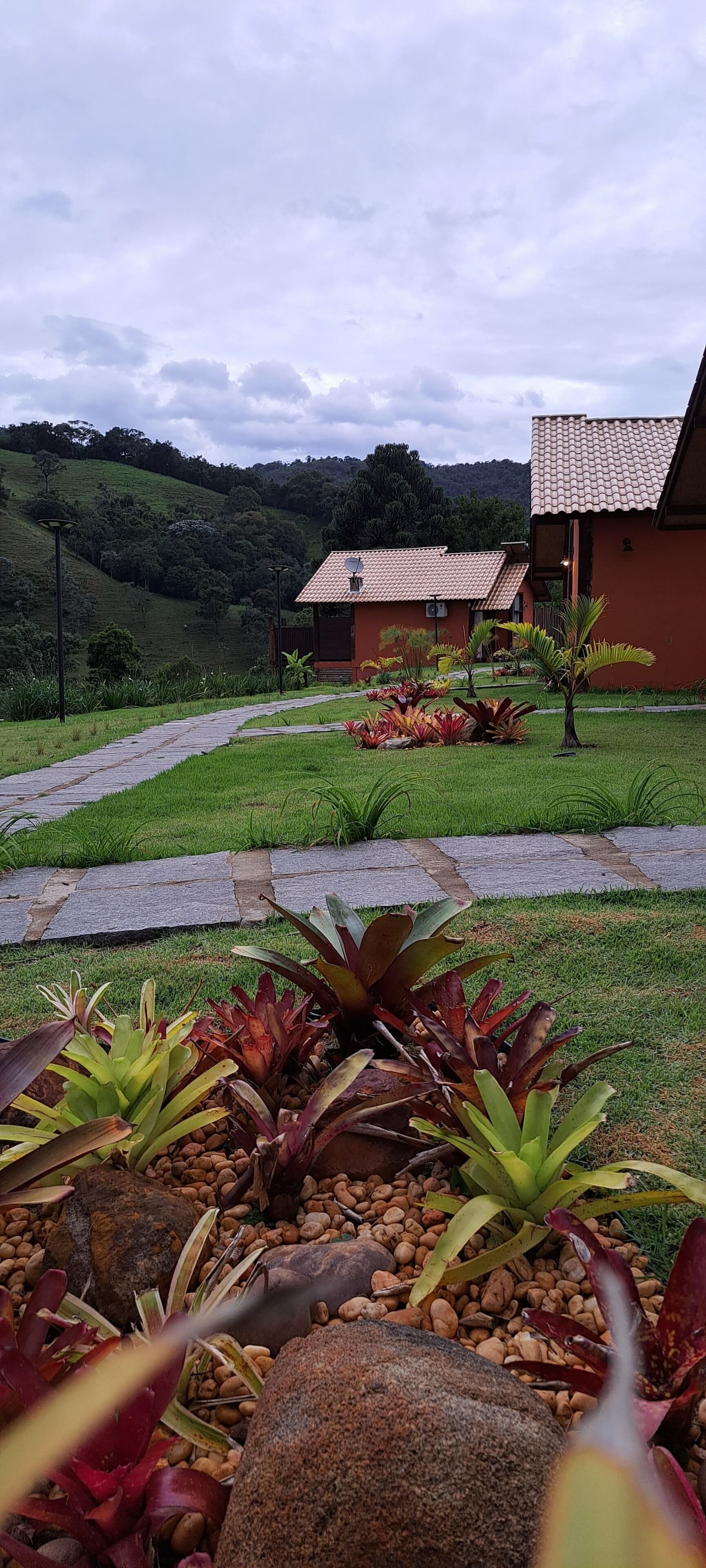 Un camino conduce a un edificio con tejado de baldosas, rodeado de un jardín ajardinado con diversas plantas y rocas.